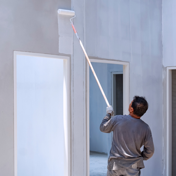 Builder painting white primer on a crete wall inside a house