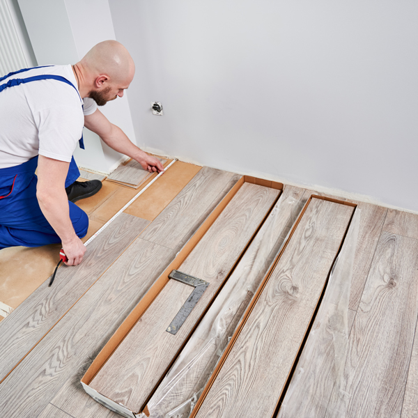 Male worker measuring distance from wall to place flooring planks